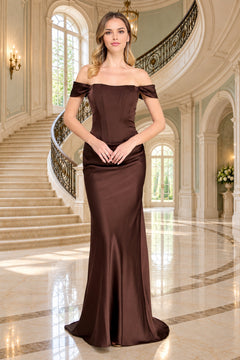 A woman stands in a grand foyer wearing an Amelia Couture 6151, an off-the-shoulder brown evening gown with a corset-style bodice.