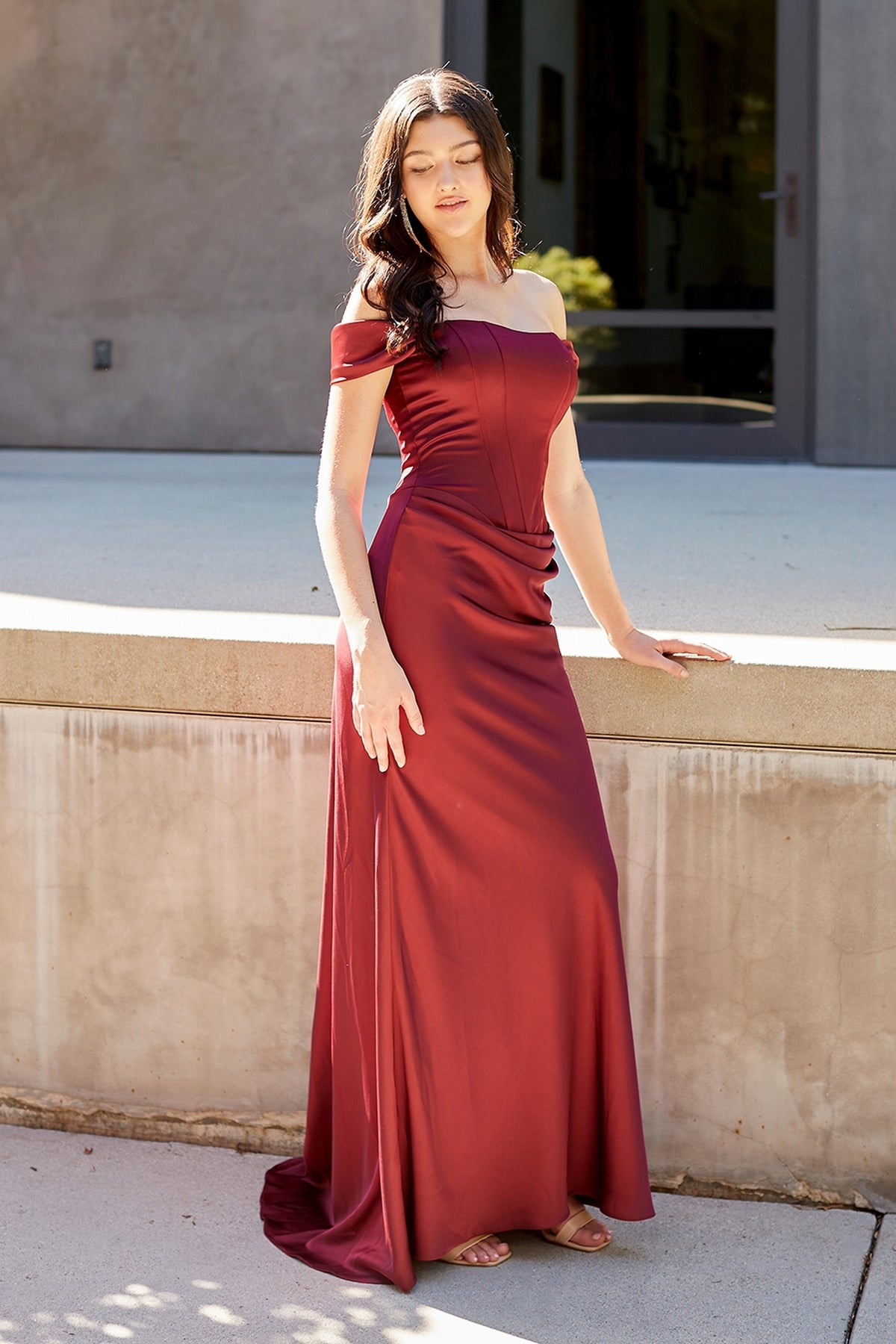 A person wearing a burgundy Amelia Couture 6151 off-the-shoulder, floor-length gown with a corset-style bodice.