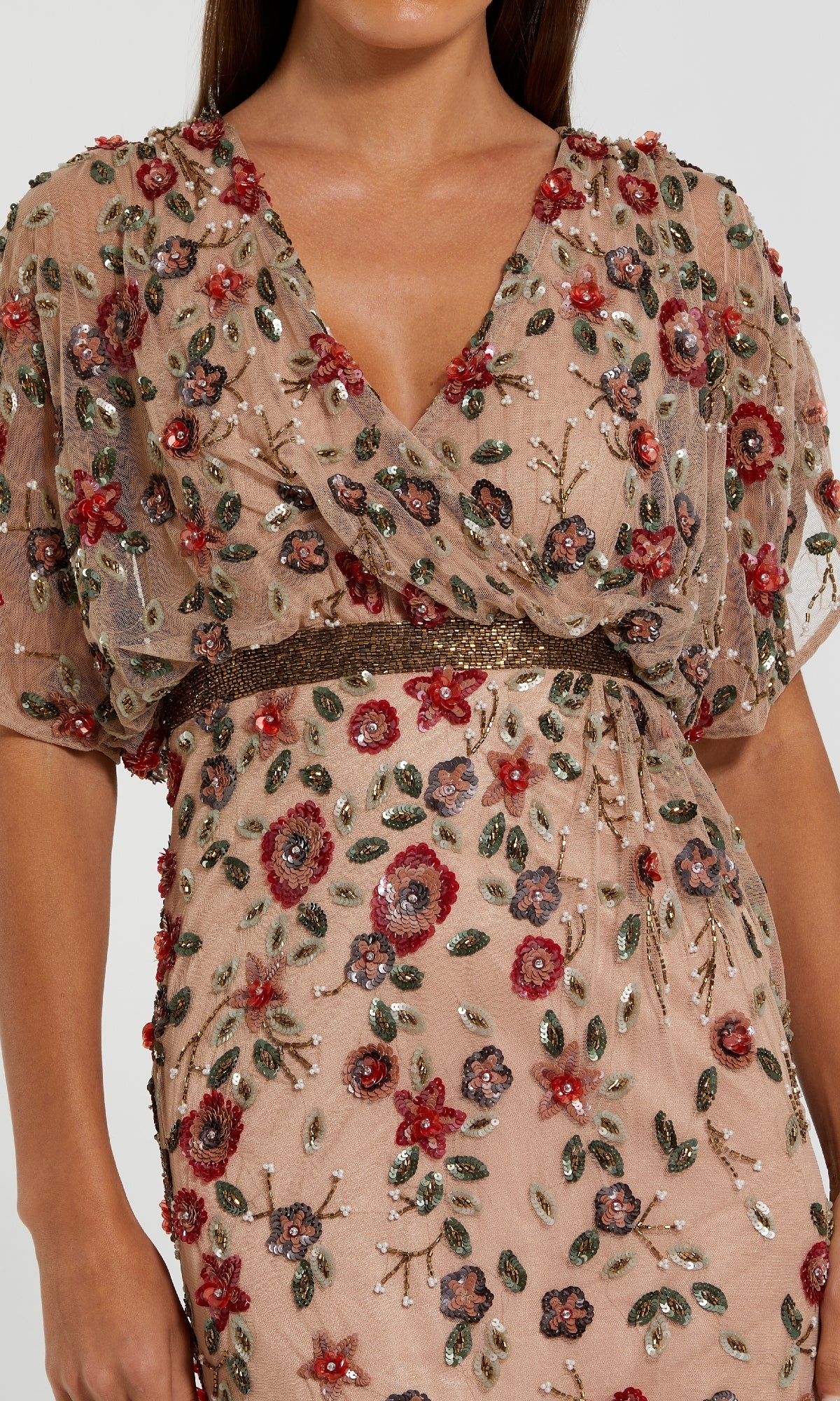 A woman wears the Mac Duggal 6158, a short sleeve beaded formal dress in sheer light brown, detailed with red, green, and purple floral beadwork and sparkling sequins.