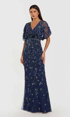 A woman wears the Mac Duggal 6158 Short Sleeve Beaded Formal Dress, a floor-length gown with sheer sleeves and multicolored floral embroidery, set against a plain white background.