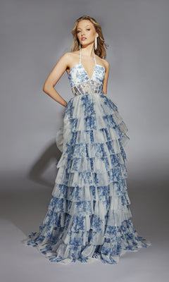 A woman wearing the Alyce 61730 Ruffled Long Print Prom Dress, featuring a sleeveless halter-neck, sheer bodice, tiered ruffled skirt, and blue floral pattern stands against a gray background.