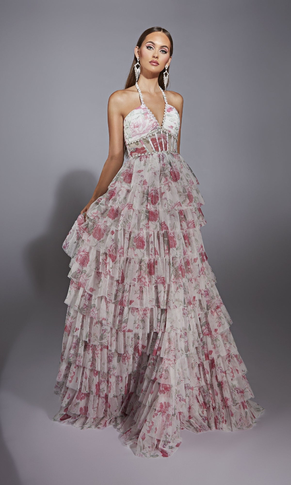 A woman poses against a gray background wearing the Alyce 61730 Ruffled Long Print Prom Dress, featuring a halter-neck, layered ruffles, and a pink floral print.
