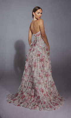 A woman wearing the Alyce 61730 Ruffled Long Print Prom Dress—strapless, floor-length, and tiered with a pink floral pattern—stands turned slightly to the side against a plain gray background.