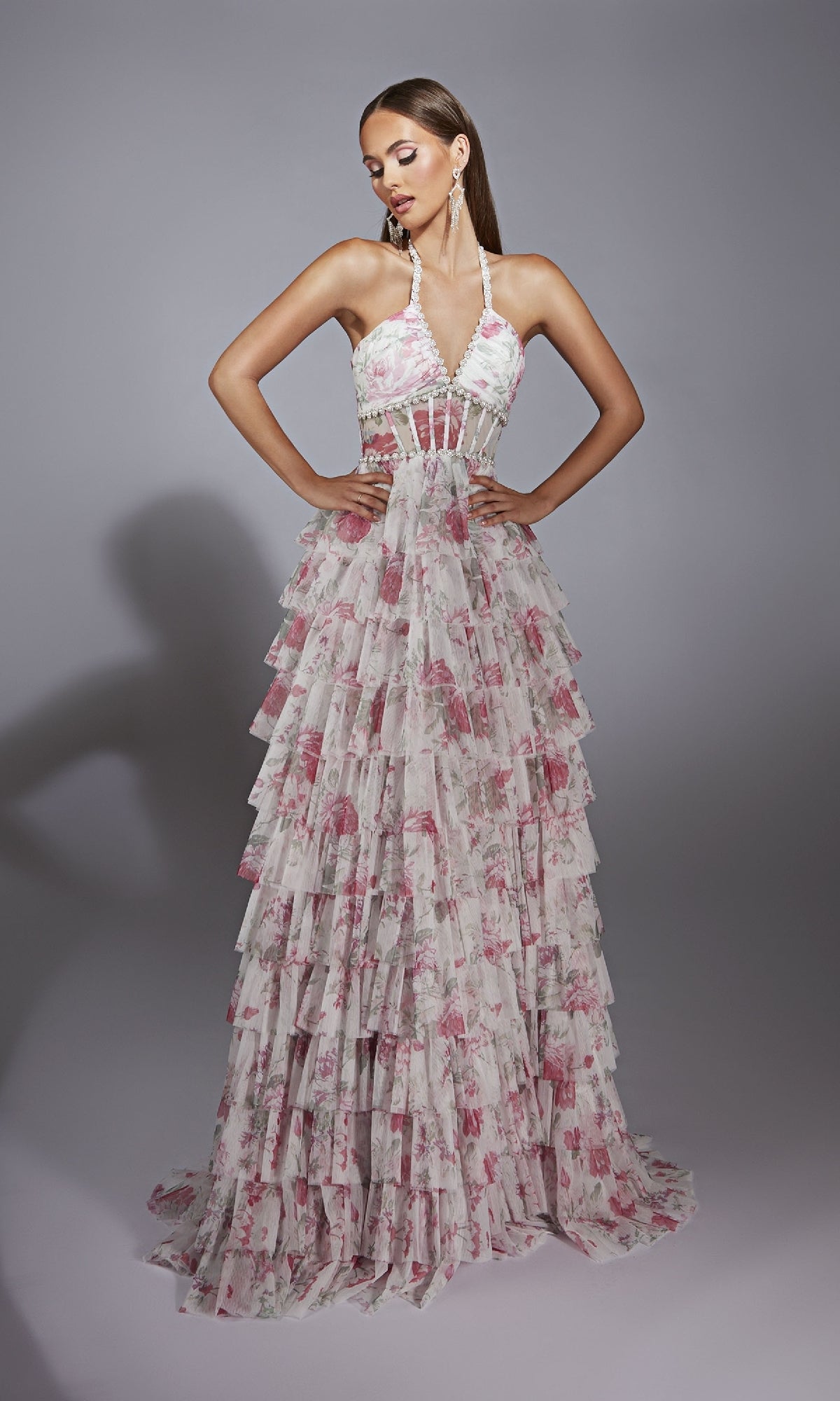 A woman poses confidently with her hands on her waist, modeling the Alyce 61730 Ruffled Long Print Prom Dress featuring a pink floral pattern and halter neckline against a plain background.