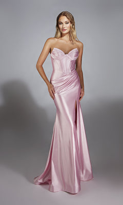 A woman wears the Alyce 61733 Strapless Long Corset Prom Dress in pale pink satin, featuring a fitted silhouette, sweetheart neckline, and high slit, standing against a plain gray background.
