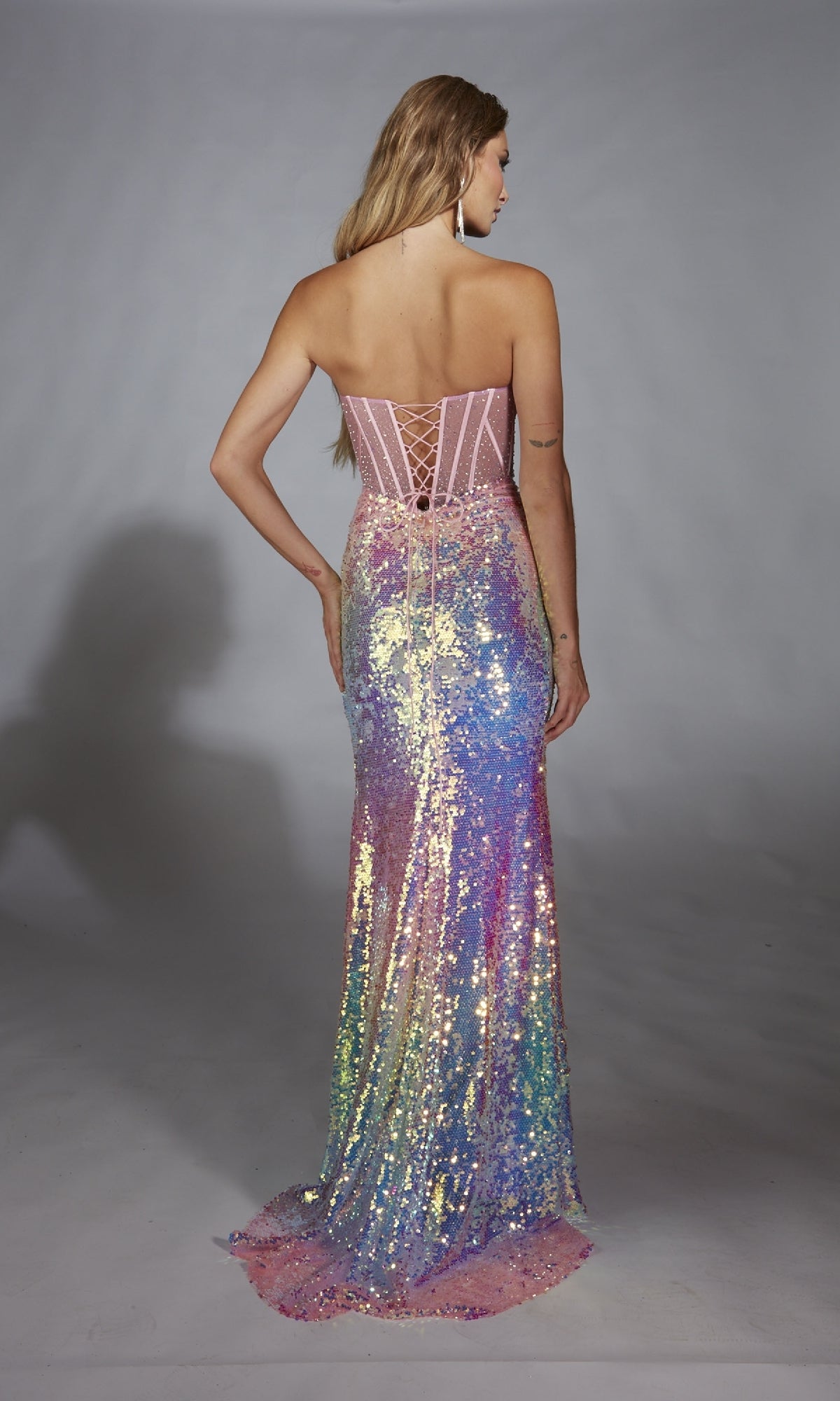 A woman faces away from the camera in the Alyce 61734 long prom dress, a strapless gown adorned with iridescent pink, purple, blue, and yellow sequins.