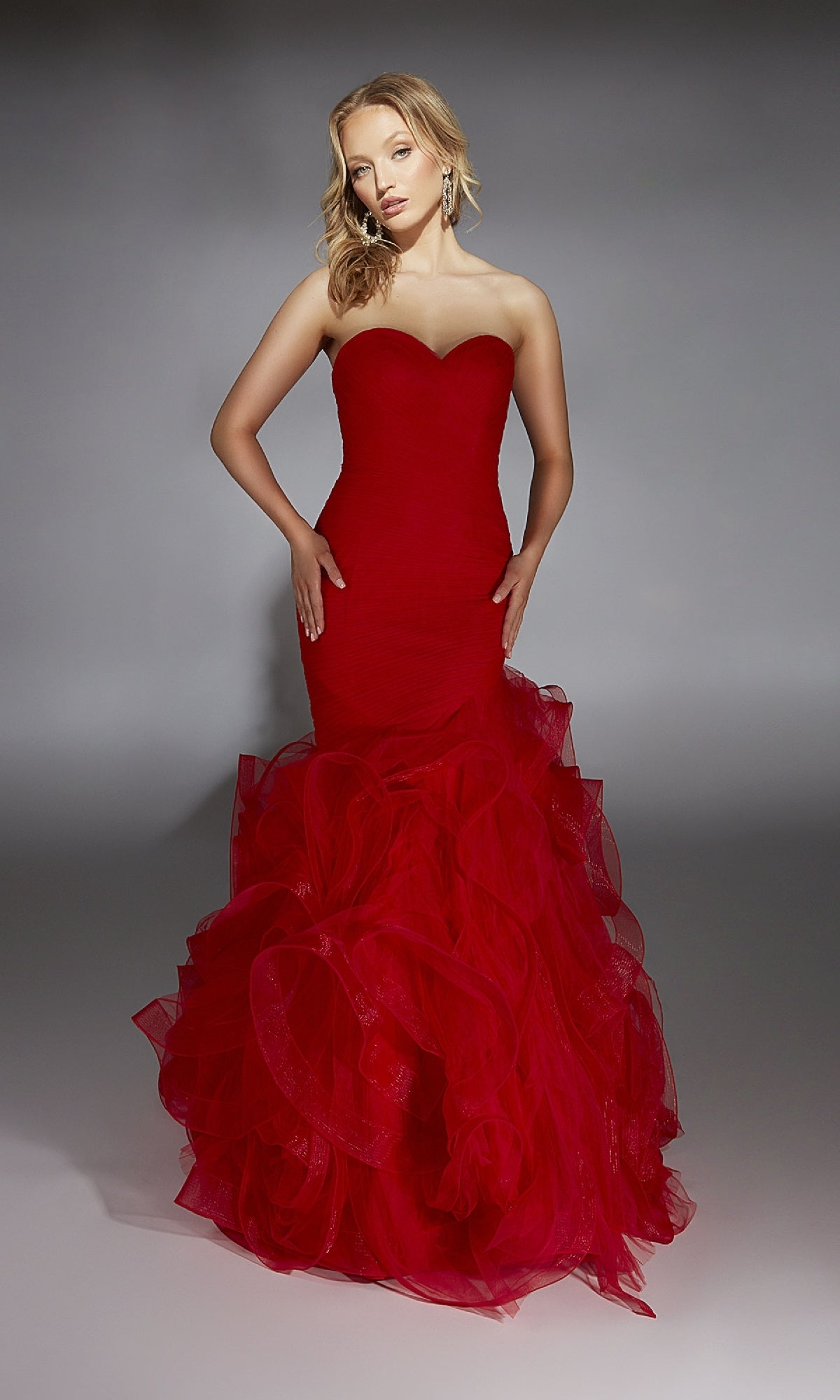 A woman wears the Alyce 61739 long prom dress featuring a strapless mermaid silhouette, sweetheart neckline, and ruffled tulle skirt, set against a plain gray background.