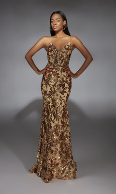 A woman stands with hands on hips in the Lace-Up Long Sequin Prom Dress: Alyce 61755, a fitted, floor-length gold gown with sequined floral patterns, against a plain gray background.