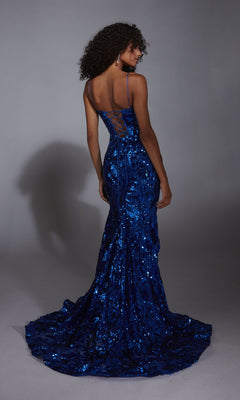 A woman in the Lace-Up Long Sequin Prom Dress: Alyce 61755, featuring a floor-length blue sequin design, fitted bodice, and lace-up back, stands facing away from the camera.