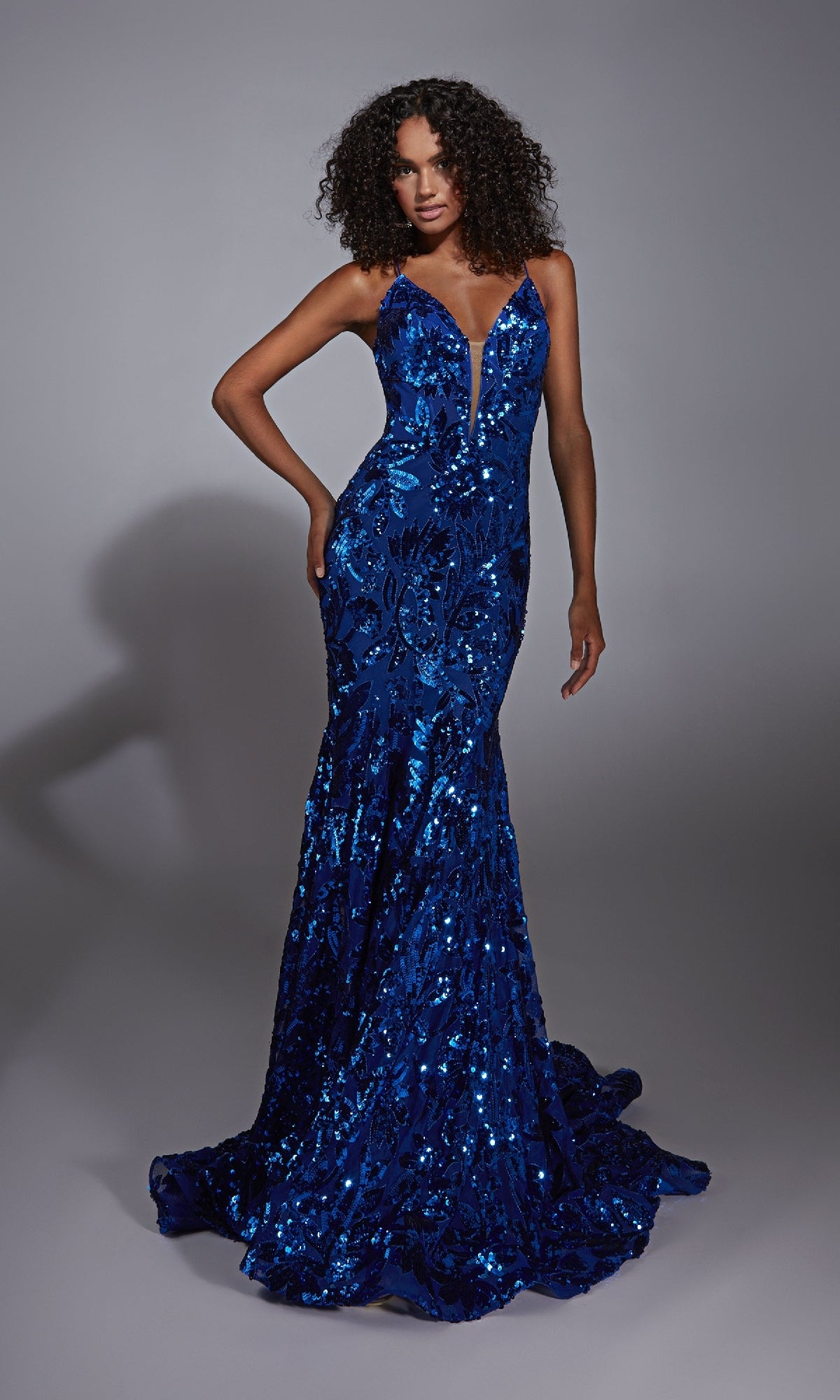 A woman poses against a plain backdrop in the Alyce 61755 Lace-Up Long Sequin Prom Dress, featuring a fitted, floor-length deep blue design with a v-neckline and thin straps.