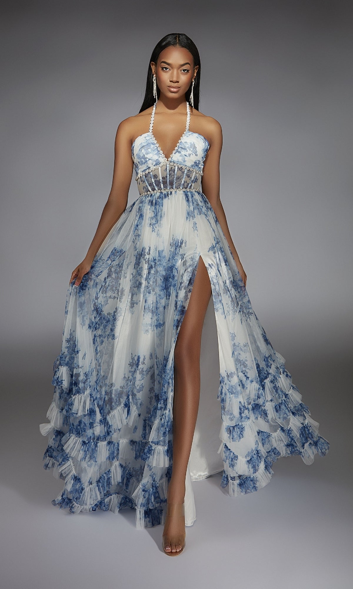 A woman poses in the floor-length Alyce 61757 long prom dress, featuring blue floral patterns, a sheer bodice, and a high leg slit.