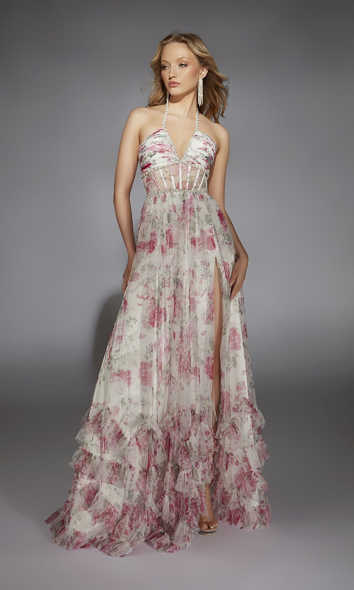 A woman poses against a gray background in the Alyce 61757 long prom dress, featuring a sleeveless floral-print design with a halter neckline, sheer bodice, and ruffled hem.