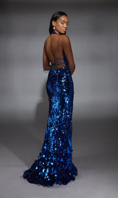 A woman models the Alyce 61759 Halter V-Neck Sequin Long Prom Dress, a shimmering blue, backless gown, as she stands in a studio and looks over her shoulder.