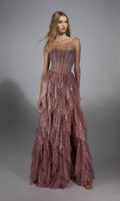 A woman wears the Alyce 61762 Strapless Long Glitter A-Prom Dress featuring ruffles and a sheer, beaded bodice, standing against a plain gray background.