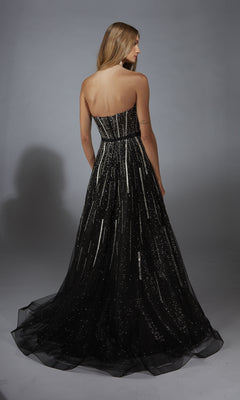 A woman with long blonde hair, facing away from the camera, models the Alyce 61770 long prom dress—a strapless glitter gown with a corset bodice—against a plain gray background.
