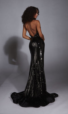A woman with curly hair stands on a plain backdrop, facing away from the camera, wearing the Alyce 61772 long prom dress—a floor-length, backless sequin gown.
