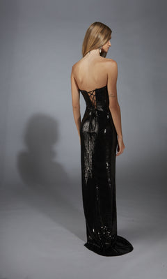 A woman faces away on a plain gray background wearing the Alyce 61773: a strapless long sequin prom dress with a corset-style bodice and lace-up back.