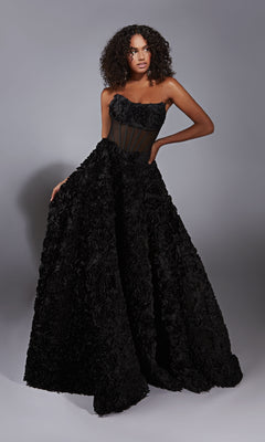 A woman models the Alyce 61775 Strapless Rosette Prom Ball Gown, featuring a corset-style bodice and textured floral skirt, while standing against a plain gray background.