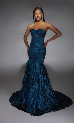 A woman models the Alyce 61782 long prom dress—a strapless, dark blue mermaid gown with ruffled layers and a keyhole neckline—posing with one hand on her hip against a plain gray background.
