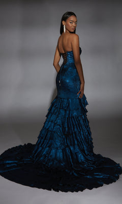 A woman models the Alyce 61782 long prom dress—strapless, dark blue mermaid style with ruffled layers and a sweeping train—posing elegantly against a plain gray background.