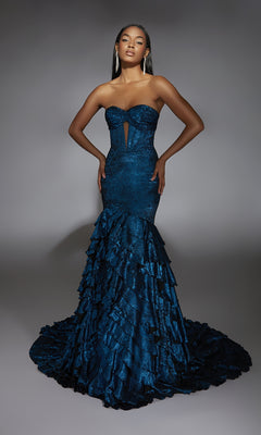 A woman models the Alyce 61782 long prom dress, a strapless dark blue mermaid gown with ruffled layers, a front cutout, and a modern fitted silhouette, standing against a plain gray background.