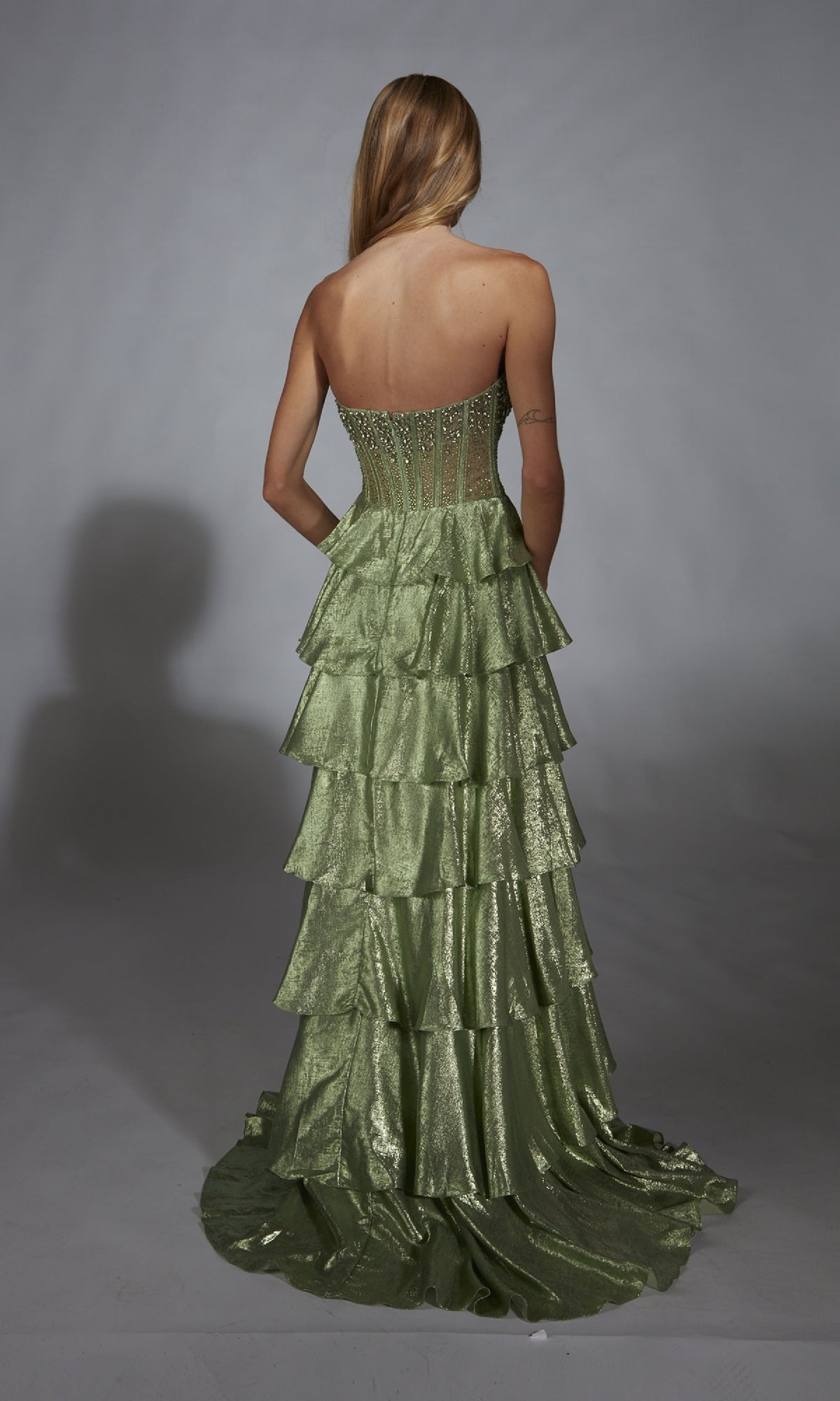 A woman faces away, wearing the Alyce 61783 long prom dress with a strapless embellished corset bodice and shimmery green tiered A-line skirt, featuring a fitted, partially sheer design.