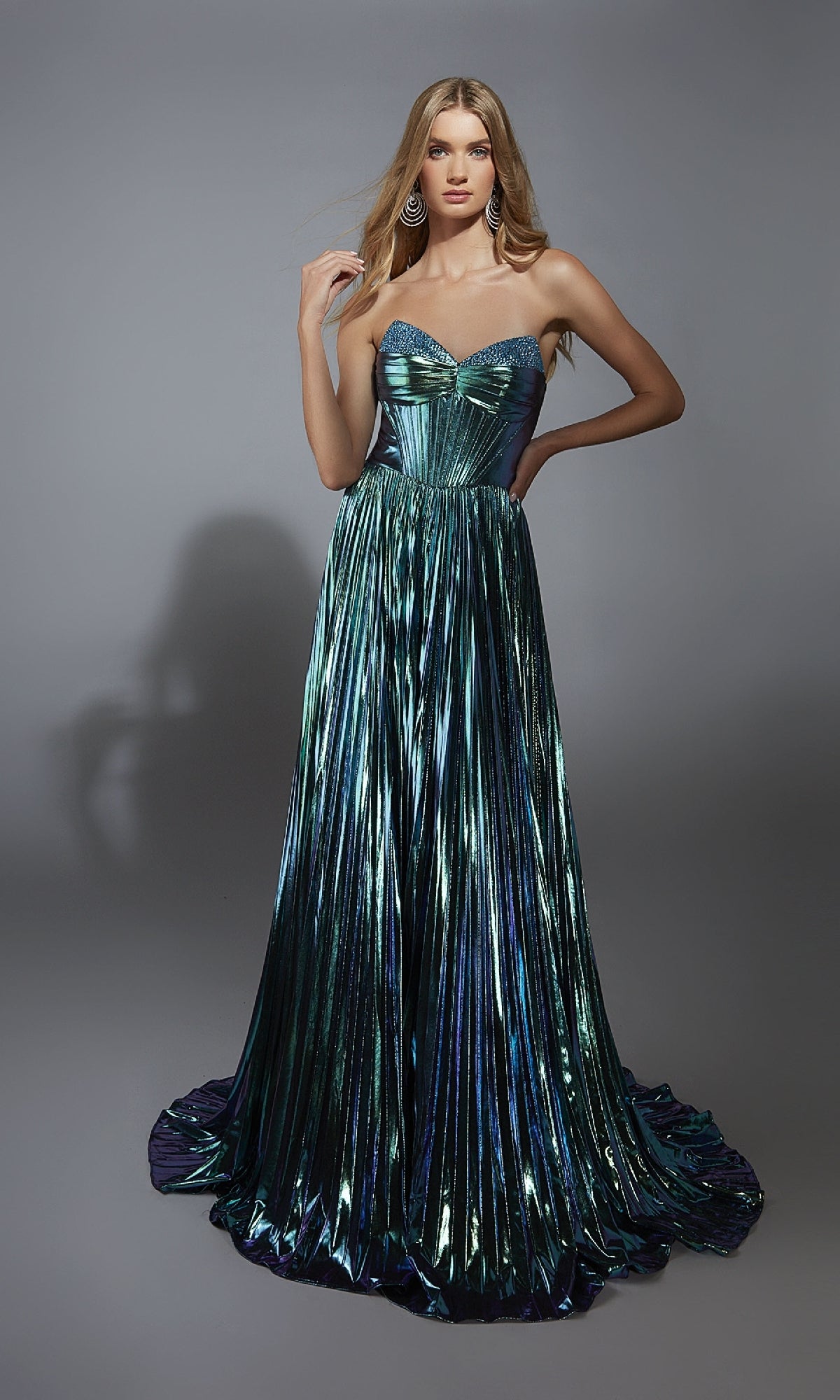A woman poses against a gray background in the Alyce 61786 Strapless Pleated Metallic Prom Gown, showcasing green and blue pleats in a floor-length, strapless design.