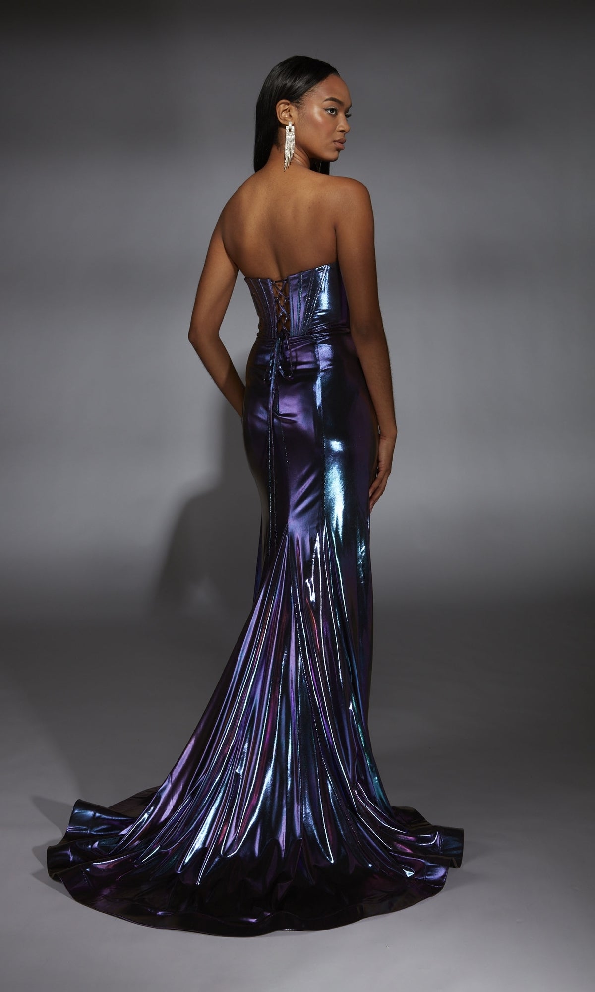 A woman stands facing away against a gray background, wearing the Alyce 61798 Strapless Metallic Long Prom Dress in purple with a long train.