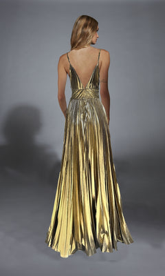 A woman faces away in the Alyce 61804 Long Prom Dress, showcasing its metallic gold finish, pleated A-line skirt, and flowing floor-length design against a neutral backdrop.