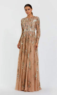A woman stands facing forward, wearing the Mac Duggal 6181 long formal dress in taupe—a floor-length, long-sleeved gown adorned with silver sequins and bead embellishments. The background is plain white.