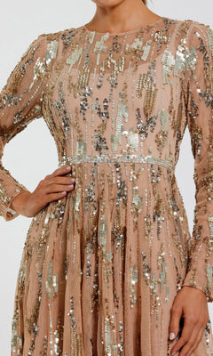 A woman poses with one hand on her hip, wearing the elegant Mac Duggal 6181 long formal dress—a blush-colored, long-sleeve gown adorned with gold and silver sequins in striking abstract patterns, perfect for evening occasions.