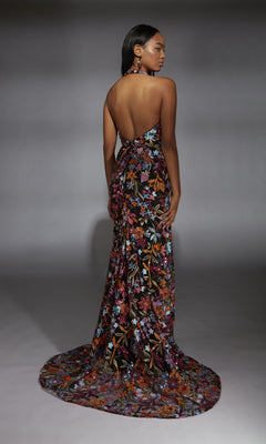 A woman stands on a gray background, facing away, wearing the Alyce 61813 long prom dress—backless, floor-length with a floral sequin design and train.