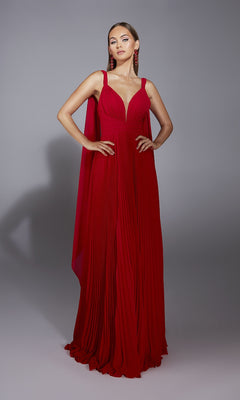 A woman stands in a studio against a gray background wearing the Alyce 61823 long red prom dress with pleats, deep V-neckline, and matching red earrings, her hands on her hips.