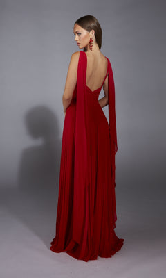 A woman wearing the Alyce 61823 long prom dress with a v-neckline and draped red fabric, paired with matching red earrings, stands facing away against a plain gray background.
