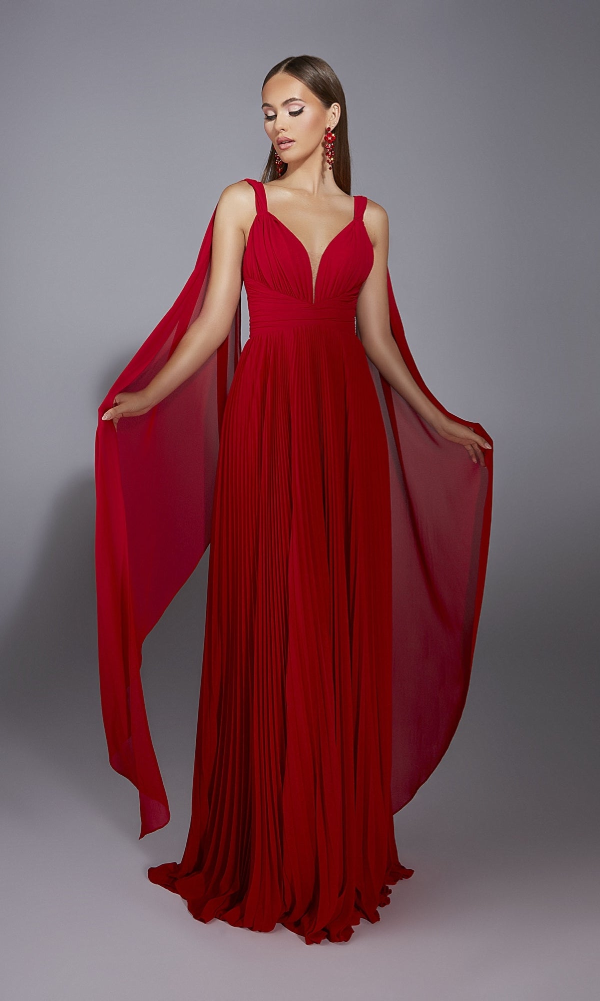 A woman models the Alyce 61823 long prom dress, featuring a sleeveless v-neck design and flowing chiffon panels cascading from the shoulders.