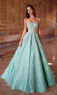 A woman wears the Long Prom Dress: Alyce 61824, a light blue-green ball gown with floral embroidery and a corset bodice, standing indoors on a marble floor with ornate wall decor in the background.
