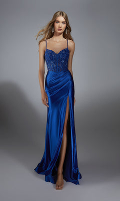 A woman in the Alyce 61827 Beaded-Corset Long Prom Dress—a blue, floor-length gown with a beaded bodice, thin straps, and a high slit—stands against a plain gray background.