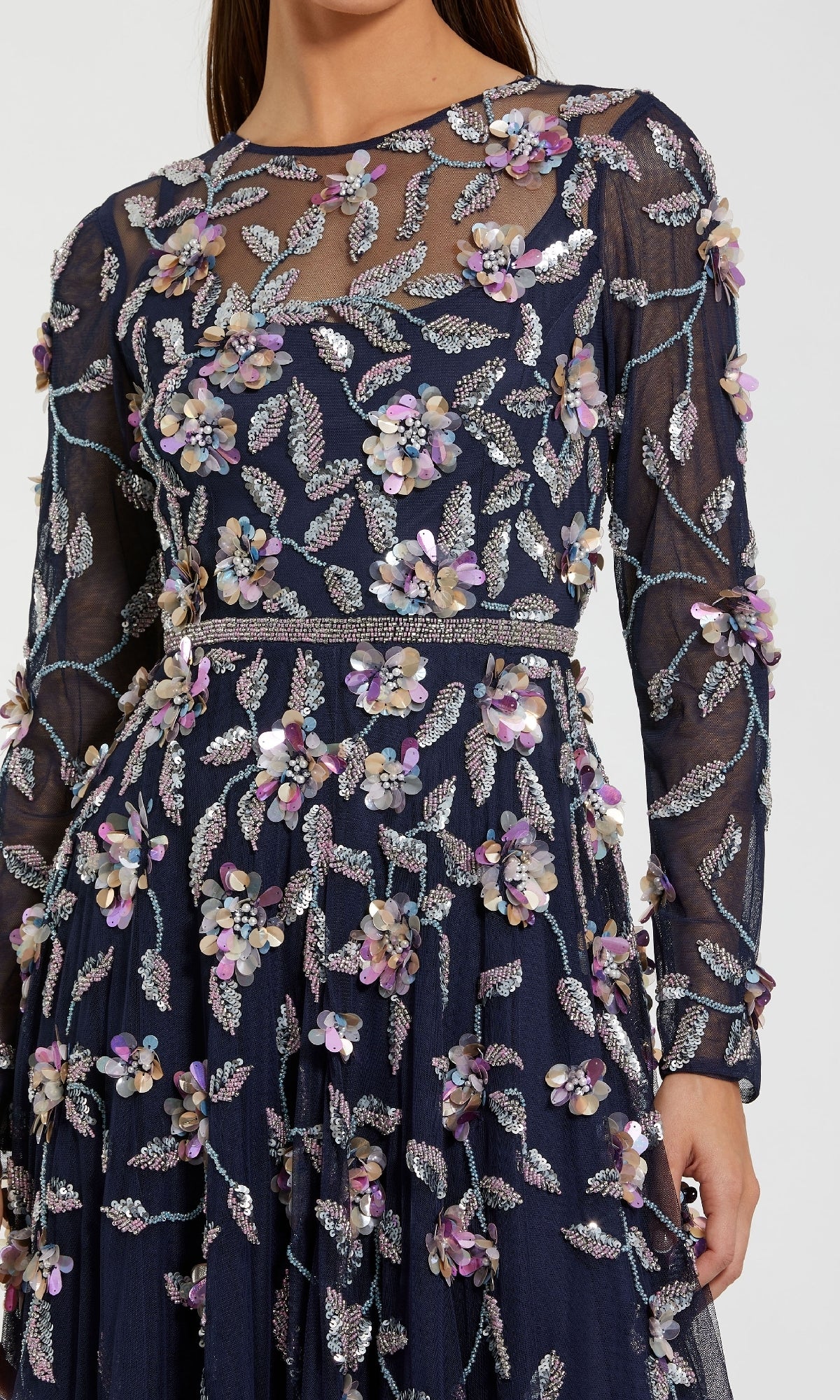A woman wears a navy blue Mac Duggal 6183 Long Sleeve Beaded Formal Gown, featuring silver leaf and purple floral appliqué embroidery.