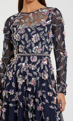 A woman wears a navy blue Mac Duggal 6183 Long Sleeve Beaded Formal Gown, featuring silver leaf and purple floral appliqué embroidery.