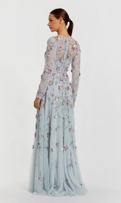 A woman stands in profile wearing the Mac Duggal 6183 Long Sleeve Beaded Formal Gown, a light blue floor-length dress adorned with floral appliqué detailing.