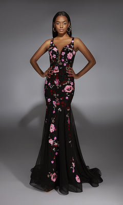 A woman stands with hands on hips, wearing the Long Prom Dress: Alyce 61839—a fitted black mermaid dress with pink and red floral details—against a plain gray background.