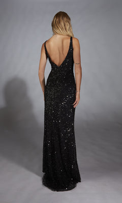 A person in the Alyce 61841 long black prom dress, featuring a floor-length sleeveless design and deep V-back, stands facing away from the camera against a gray background.