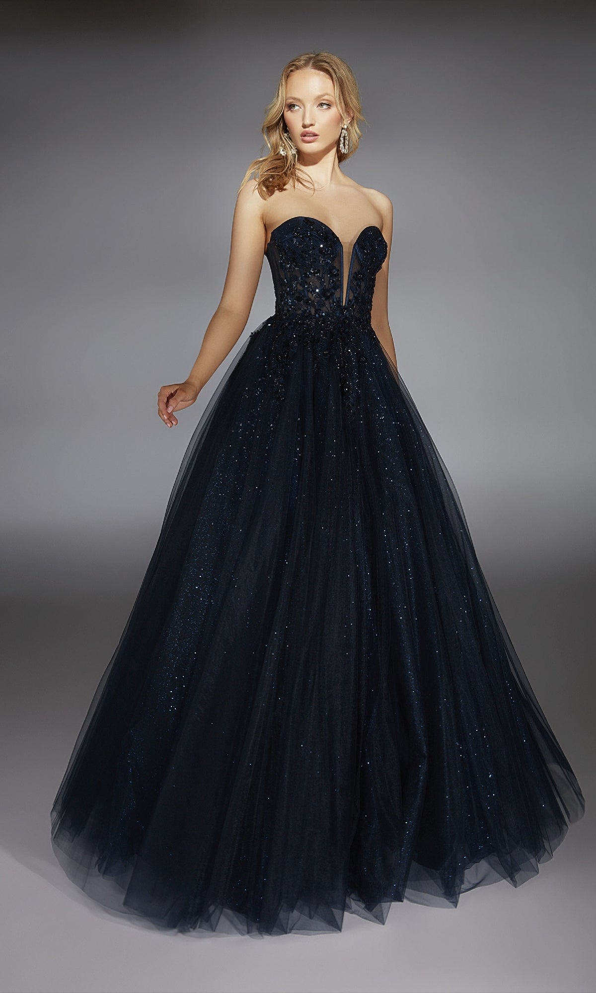 A woman stands against a gray background wearing the Alyce 61846 Strapless Long Glitter Prom Ball Gown, featuring a fitted bodice and tulle floor-length skirt.