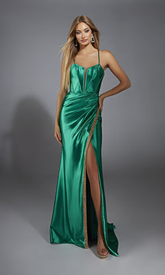 A woman poses against a gray background wearing the Alyce 61849 long prom dress—shiny green metallic stretch satin, spaghetti straps, corset bodice, and a thigh-high slit.