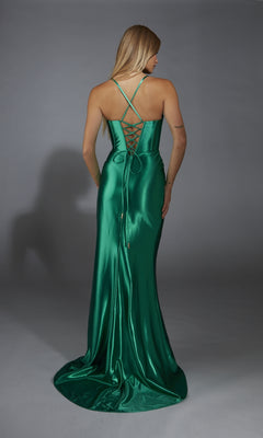 A woman stands facing away from the camera in a shiny green Alyce 61849 long prom dress featuring metallic stretch satin, spaghetti straps, and a lace-up back against a plain background.