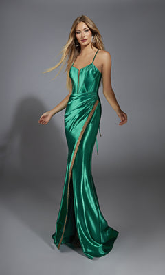 A woman poses against a plain gray backdrop wearing the Alyce 61849 long prom dress in emerald green metallic stretch satin, featuring a fitted silhouette, thin straps, corset bodice, and gold detailing.