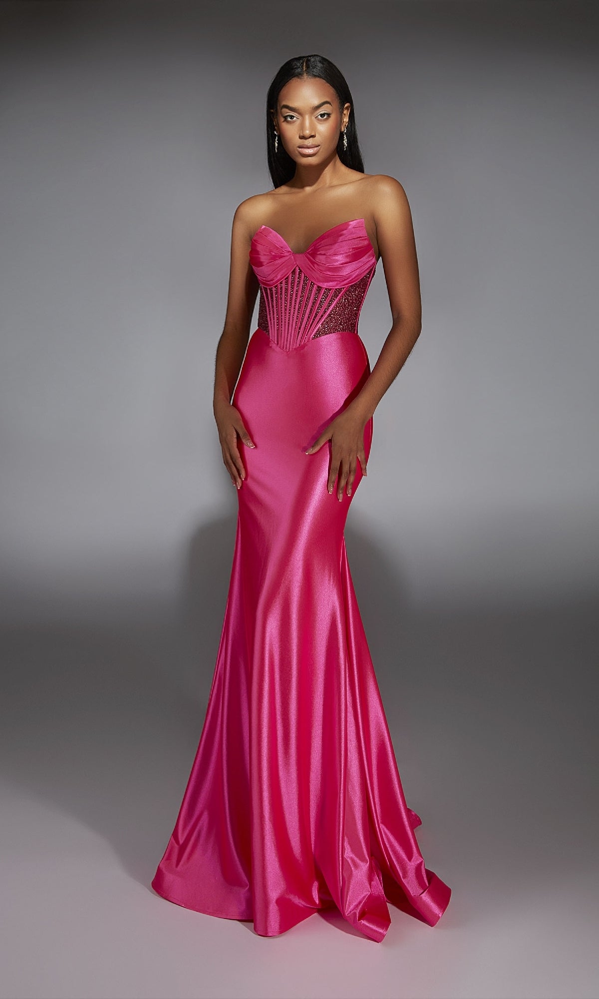 A woman models the Alyce 61851 Strapless Long Corset Prom Dress in hot pink satin, featuring a fitted bodice and flared skirt, against a plain gray background.