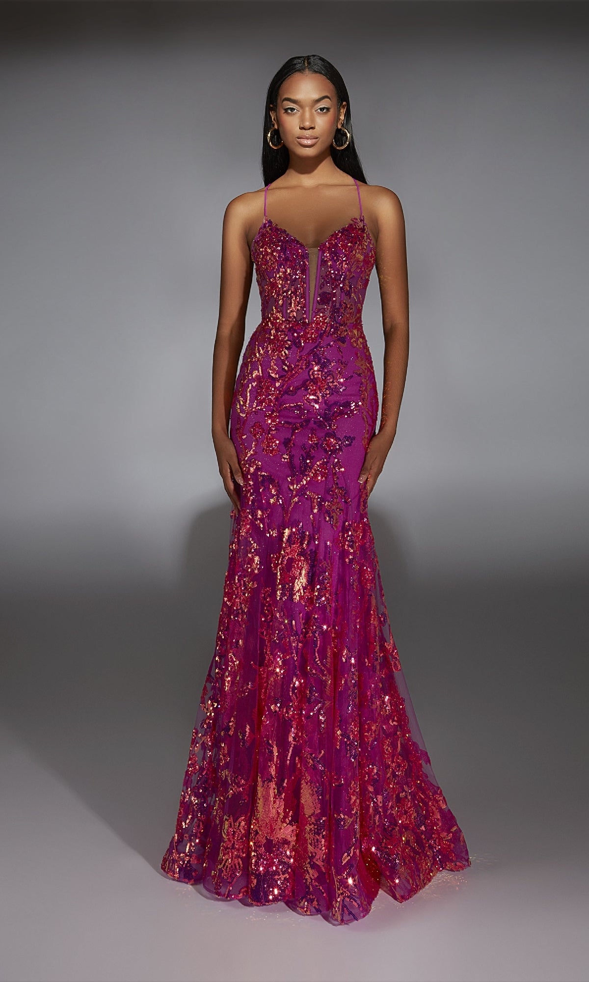 A woman wears the Alyce 61854 long prom dress, featuring neon pink sequins, thin straps, a fitted bodice, and a subtle mermaid silhouette, standing against a plain gray background.