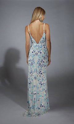 A woman faces away, modeling the Alyce Paris Long Prom Dress 61871—a floor-length, sleeveless gown with blue floral patterns and a deep V-back—set against a plain gray background.