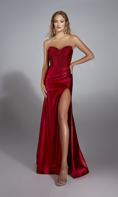 A woman poses against a plain gray background, wearing the Alyce 61884 long prom dress—strapless, floor-length metallic stretch satin with an embellished corset bodice and a high leg slit.